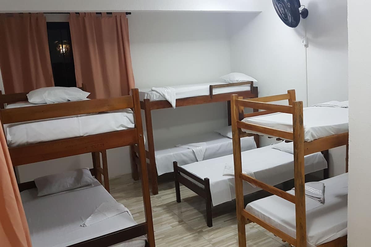 Un dormitorio con literas, ventilador de techo y ventana con cortinas.
