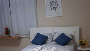 Una cama bien hecha con una colcha estampada, dos almohadas azules y una pared con una frase motivacional.