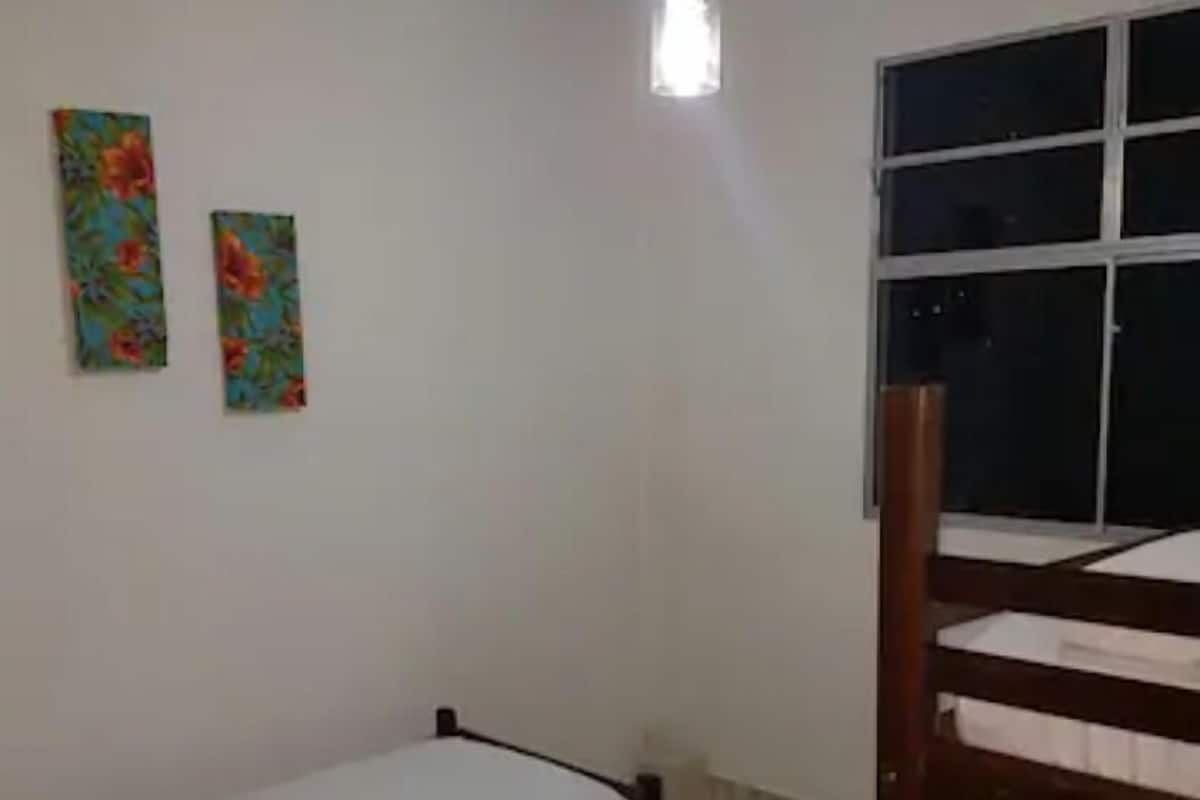 Una habitación con una litera, una cama individual, una ventana y dos cuadros con motivos florales en la pared.
