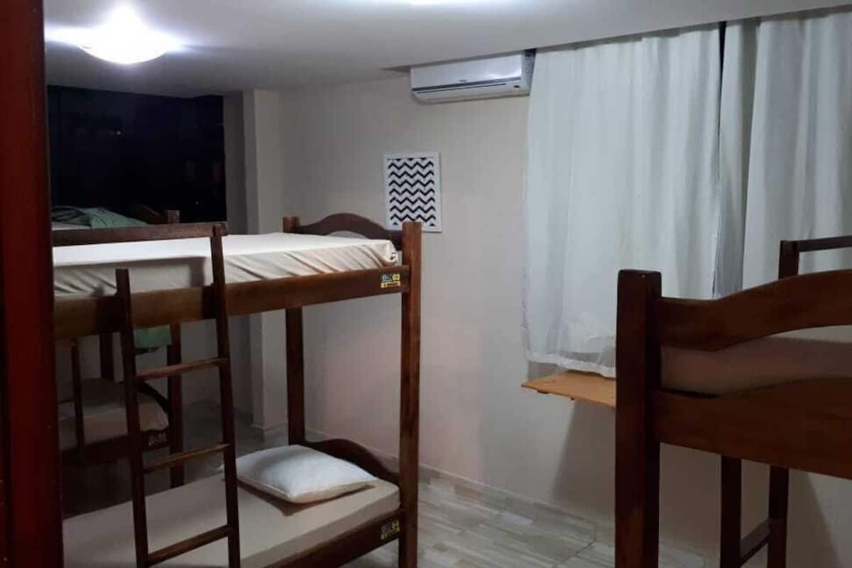 Un dormitorio con literas, una ventana con cortinas, un equipo de aire acondicionado y un cartel en la pared.
