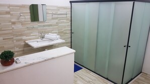 Un baño con lavamanos de mármol, cabina de ducha con mampara de vidrio y un revestimiento de pared de madera.