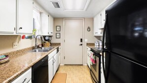 Una cocina compacta con armarios blancos, un refrigerador negro y piso de baldosas.