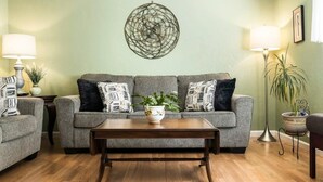 Una sala de estar con un sofá gris, dos sillones, una mesa de centro de madera y una lámpara de pie.