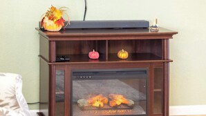 Una chimenea con puerta de cristal, un estante pequeño con calabazas decorativas y un control remoto encima.