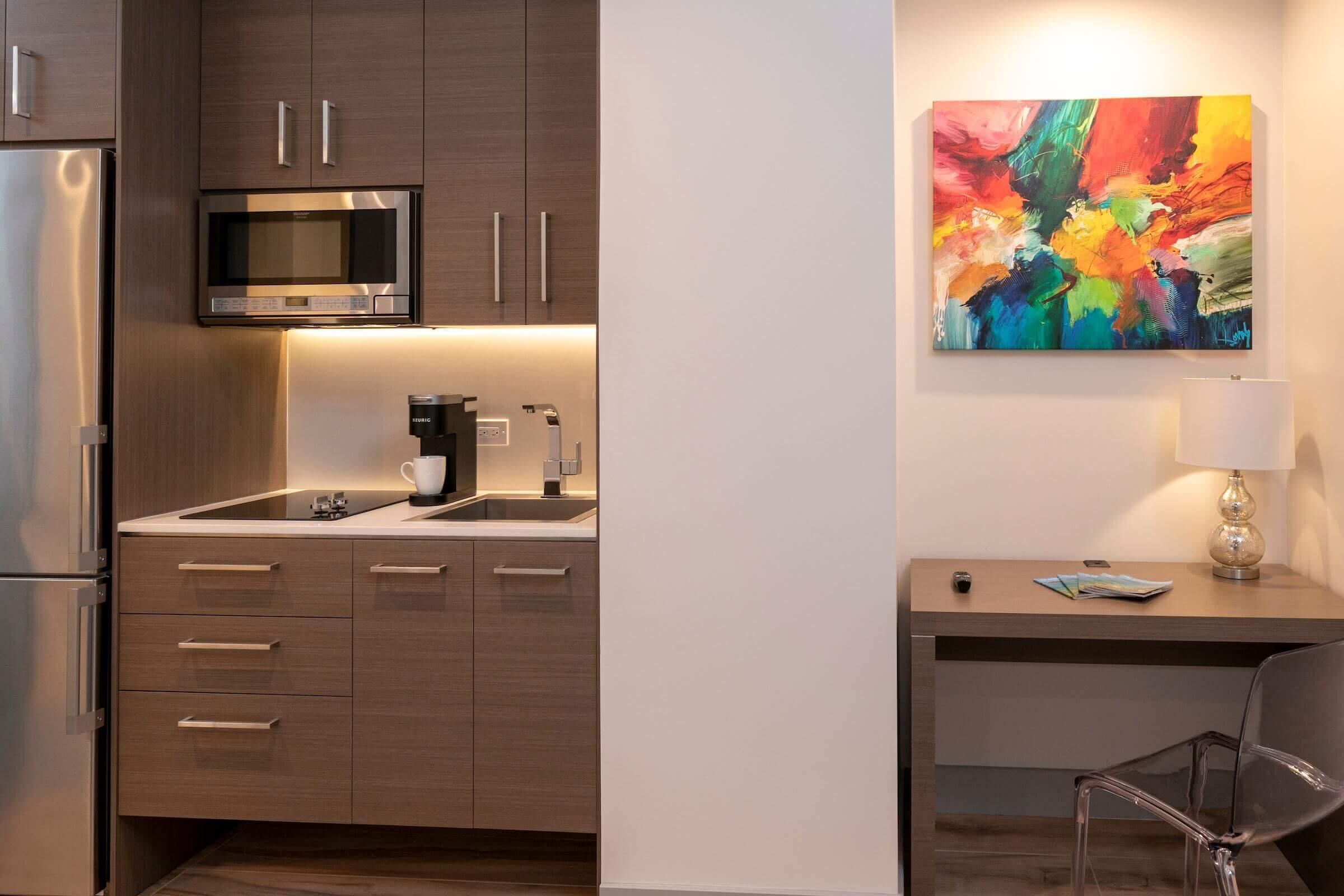 A modern kitchen with a microwave, coffee maker, and a painting on the wall.