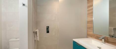 Un bagno moderno con un water bianco, box doccia in vetro, lavabo bianco con mobile contenitore in legno e uno specchio grande.