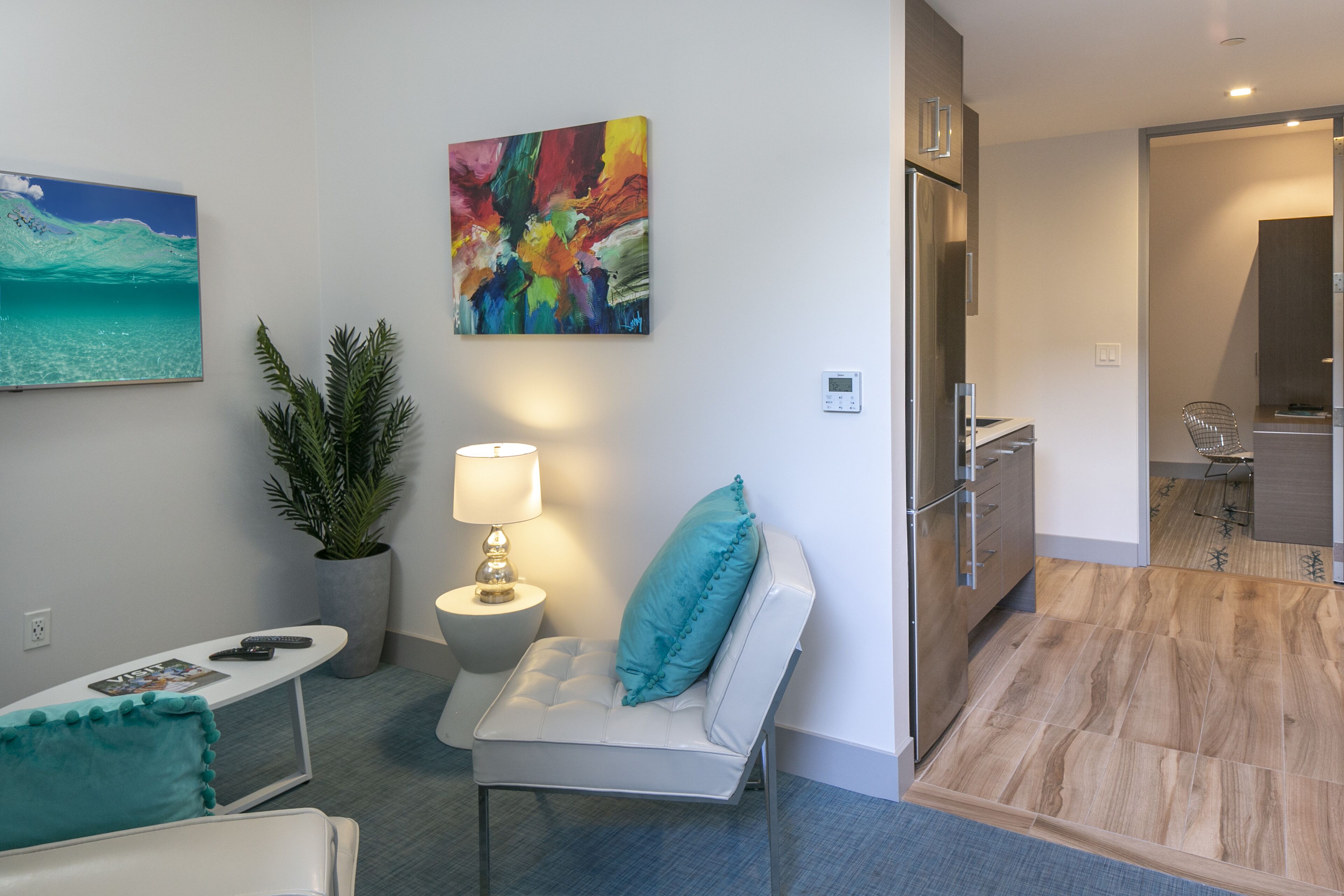 Ein modernes Wohnzimmer mit einer Couch, einem kleinen Tisch, einer Topfpflanze und einem farbenfrohen abstrakten Gemälde an der Wand.