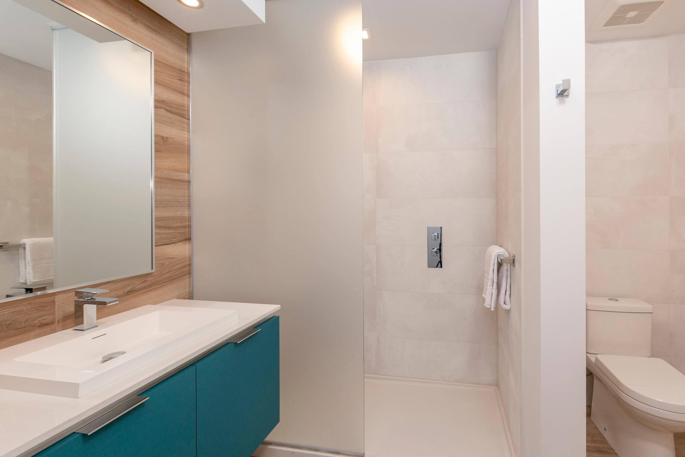 Ein modernes Badezimmer mit einem weißen Waschbecken, einem türkisblauen Schrank und einer Duschkabine aus Glas.