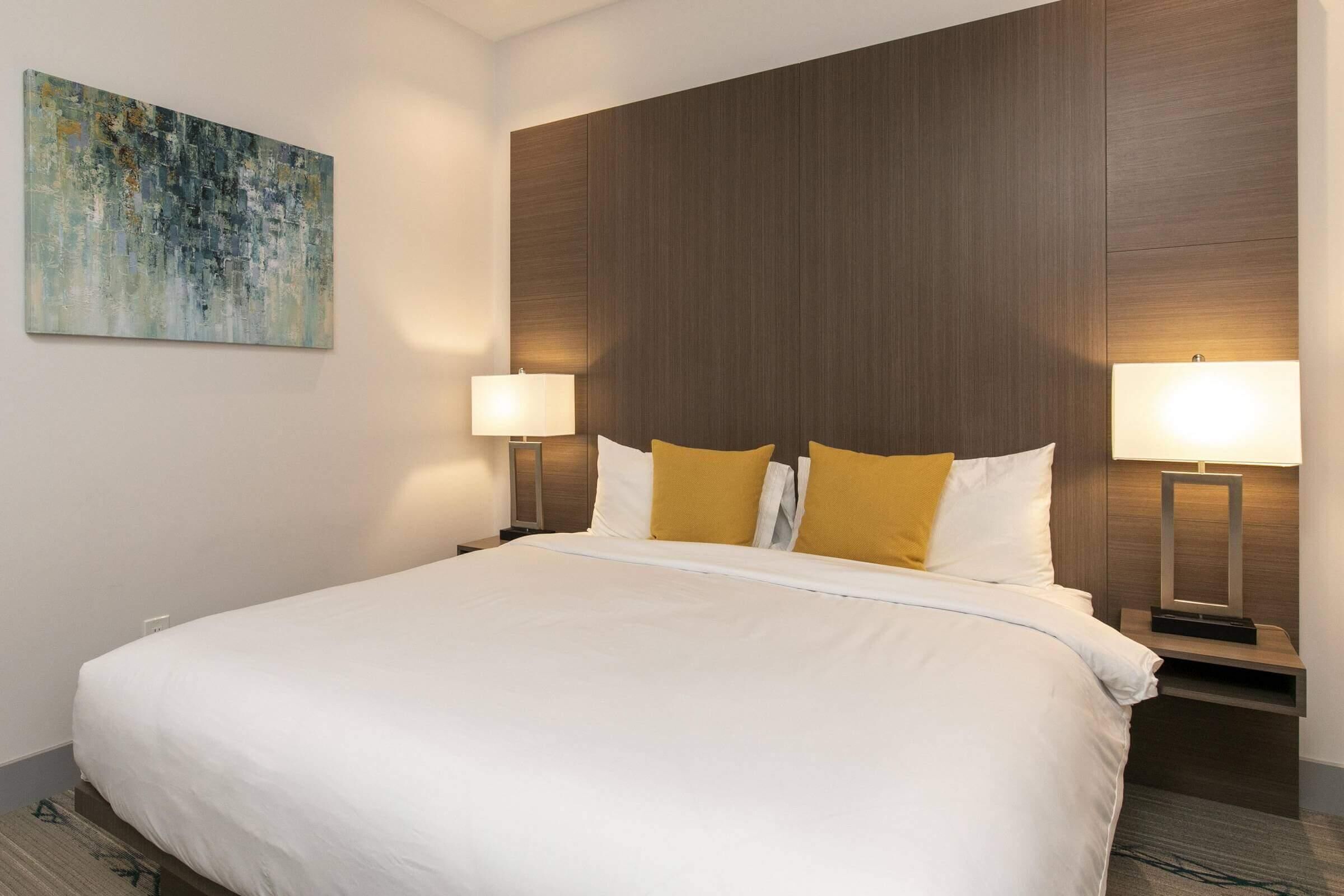 A hotel room with a large bed, two bedside lamps, and a painting on the wall.