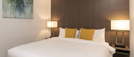 A hotel room with a large bed, two bedside lamps, and a painting on the wall.
