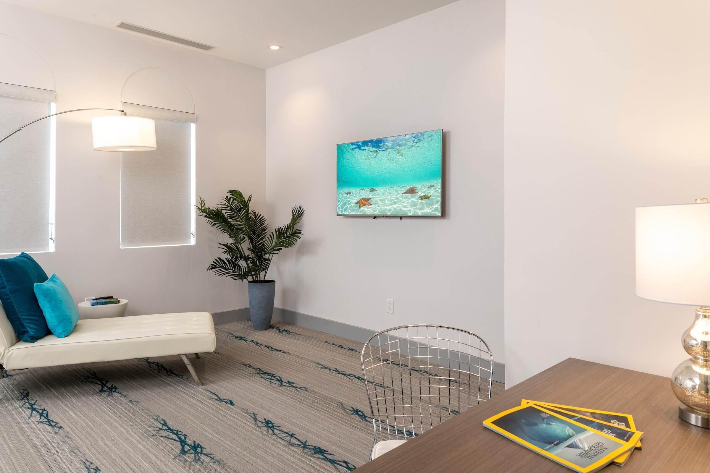 A modern living room with a sofa, a dining table with chairs, a potted plant, and a painting of an underwater scene.