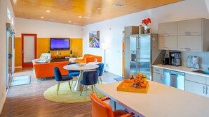 Eine moderne Küche mit Edelstahlgeräten, einem Essbereich mit orangefarbenen Stühlen und einem an der Wand montierten Flachbildfernseher.