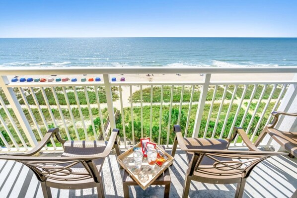 A balcony with two chairs and a table, overlooking a beach and ocean. - Need a beach getaway? Book our gorgeous Condo now! (Myrtle Beach)