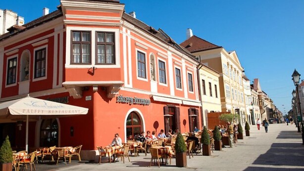 A red building with a sign for a restaurant. There are outdoor tables and chairs in front.