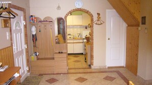 A compact kitchen with a tiled floor, a wooden door, and a clock on the wall.