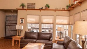 A spacious living room with a high ceiling, a ceiling fan, a brown leather sofa, a wooden coffee table, and a fireplace.