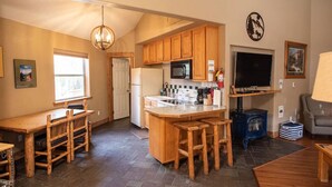 A cozy kitchen with wooden cabinets, a central island with stools, a stove, and a TV mounted on the wall.