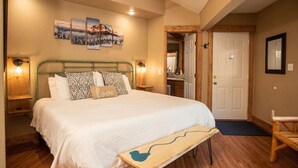 A bedroom with a large bed, a bench, and a door leading to another room.