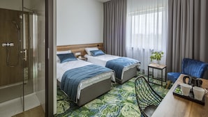 Habitación de hotel con dos camas, ducha, una mesita con una planta y una silla.