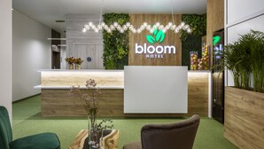 Un área de recepción de hotel moderna con un mostrador de madera, una silla verde y una pared cubierta de plantas.