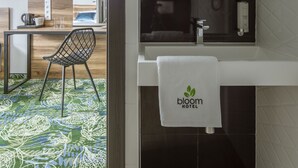 Un baño moderno con un lavamanos blanco, un espejo y una toalla con el logotipo del hotel.