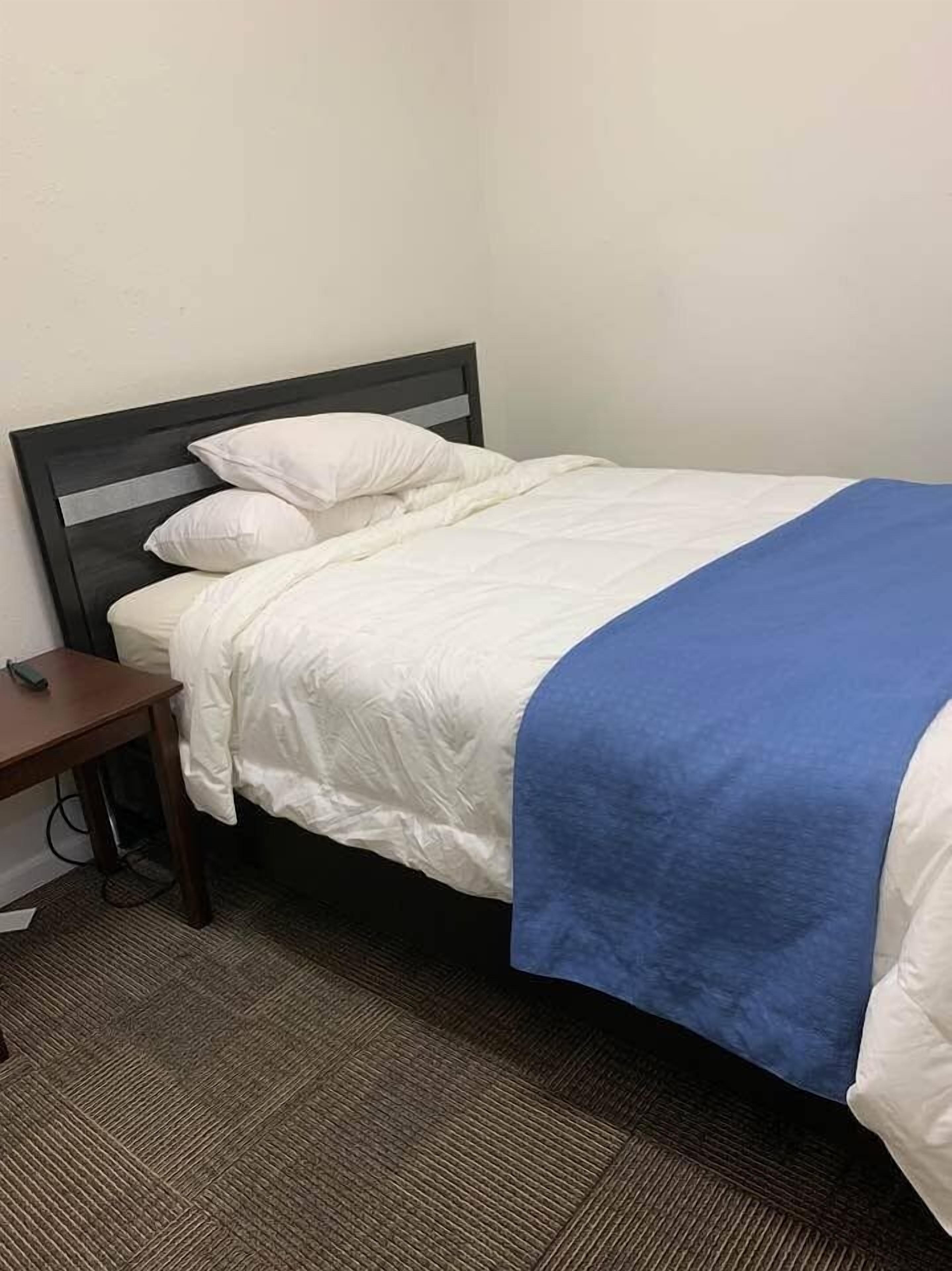 A single bed with a dark headboard, white bedding, and a blue blanket.