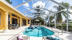 A pool area with a dolphin float, lounge chairs, and a covered patio with a view of palm trees. - Set Sail for a Spectacular Adventure - Gulf Access, Pool, Kayaks - Villa Sentio - Roelens Vacations (Cape Coral)