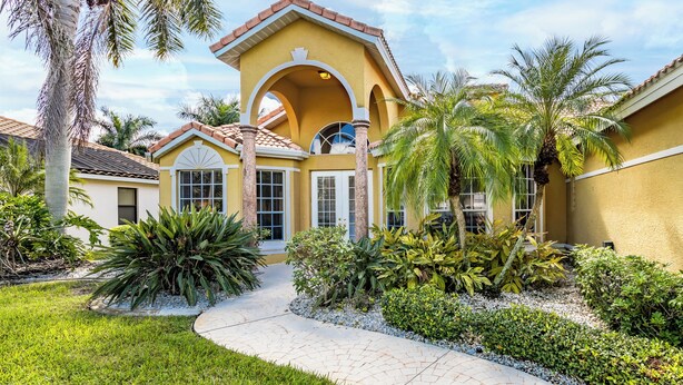 A yellow building with a tiled roof, a central archway, and a paved pathway leading to the entrance. - Set Sail for a Spectacular Adventure - Gulf Access, Pool, Kayaks - Villa Sentio - Roelens Vacations (Cape Coral)