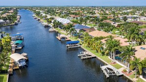 A canal lined with boats and docks, surrounded by residential houses and palm trees. - Set Sail for a Spectacular Adventure - Gulf Access, Pool, Kayaks - Villa Sentio - Roelens Vacations (Cape Coral)