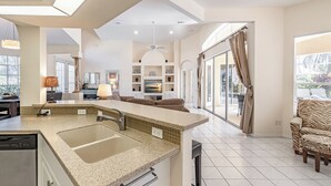 A modern kitchen with a large island, a dining area with a sofa, and a view of the outdoors. - Set Sail for a Spectacular Adventure - Gulf Access, Pool, Kayaks - Villa Sentio - Roelens Vacations (Cape Coral)