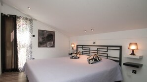 Een slaapkamer met een groot bed, twee bedlampen, een hoofdeinde, een wandplank en een gordijn.