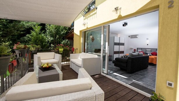 Een moderne buitenruimte met rieten meubilair, een glazen deur naar een slaapkamer en een balkon met potplanten.