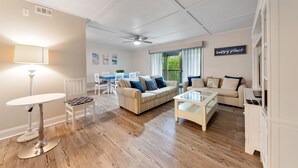 Un salon spacieux avec un plancher en bois, une table ronde, un canapé et un téléviseur.