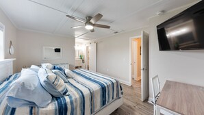 Une chambre à coucher avec un lit, un ventilateur de plafond, une télévision et un plancher en bois.