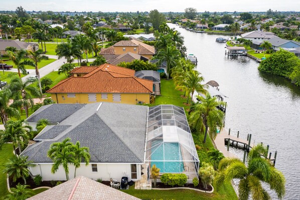 A residential area with a house featuring a swimming pool, surrounded by palm trees and a canal.