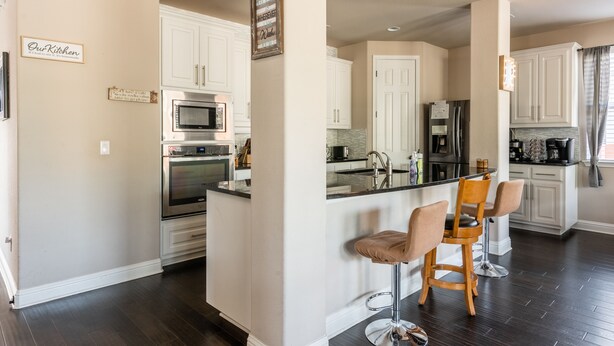 Una cocina moderna con gabinetes blancos, una isla central con taburetes de bar, electrodomésticos de acero inoxidable y un cartel que dice 'Our Kitchen'.