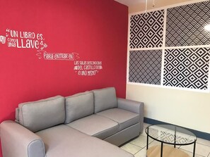 Une pièce avec un mur rouge, un canapé gris et un panneau mural à motifs.