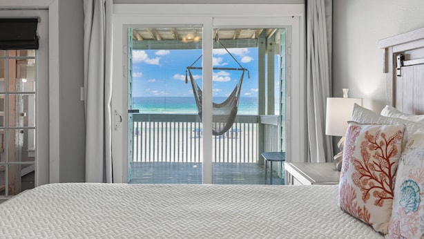 A bedroom with a bed, a hanging chair, and a view of the beach through a glass door. - BEACHFRONT Beach Vacation! Eat Breakfast While You Watch Dolphins!! (Destin)