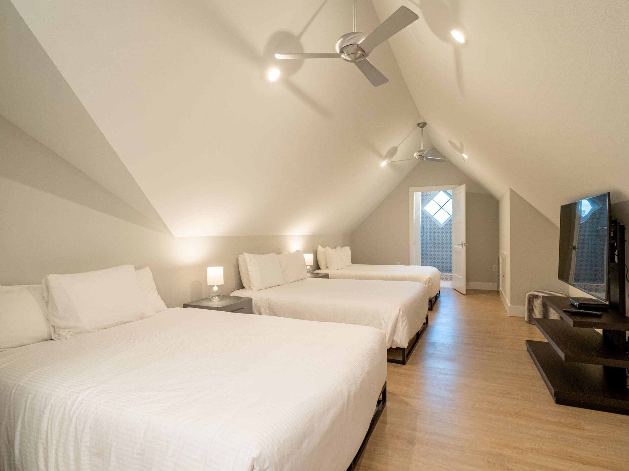 A spacious room with two beds, a ceiling fan, a TV, and a small table.