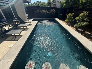 A rectangular swimming pool with clear water, surrounded by a concrete deck and a wooden fence.