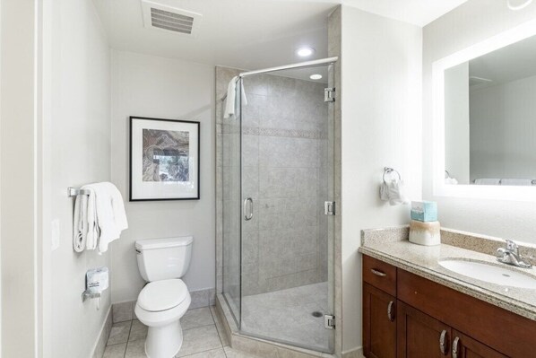 A modern bathroom with a toilet, a glass shower enclosure, a sink with a mirror, and a framed picture on the wall. - Phoenix | Desert Escape | Golf & Resort Pool (Phoenix)