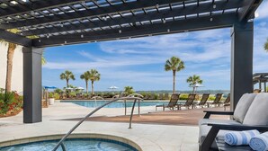 A pool area with lounge chairs, a hot tub, and a pergola with string lights.