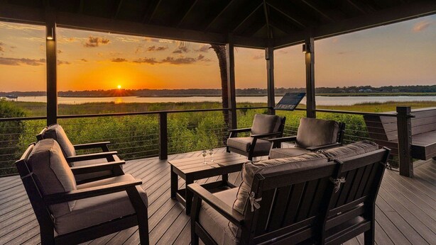A covered outdoor seating area with a view of the sunset over a body of water.