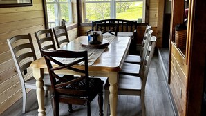 Een houten eetkamer met een grote tafel en stoelen, een raam met uitzicht op groen en decoraties van gewei aan het plafond.