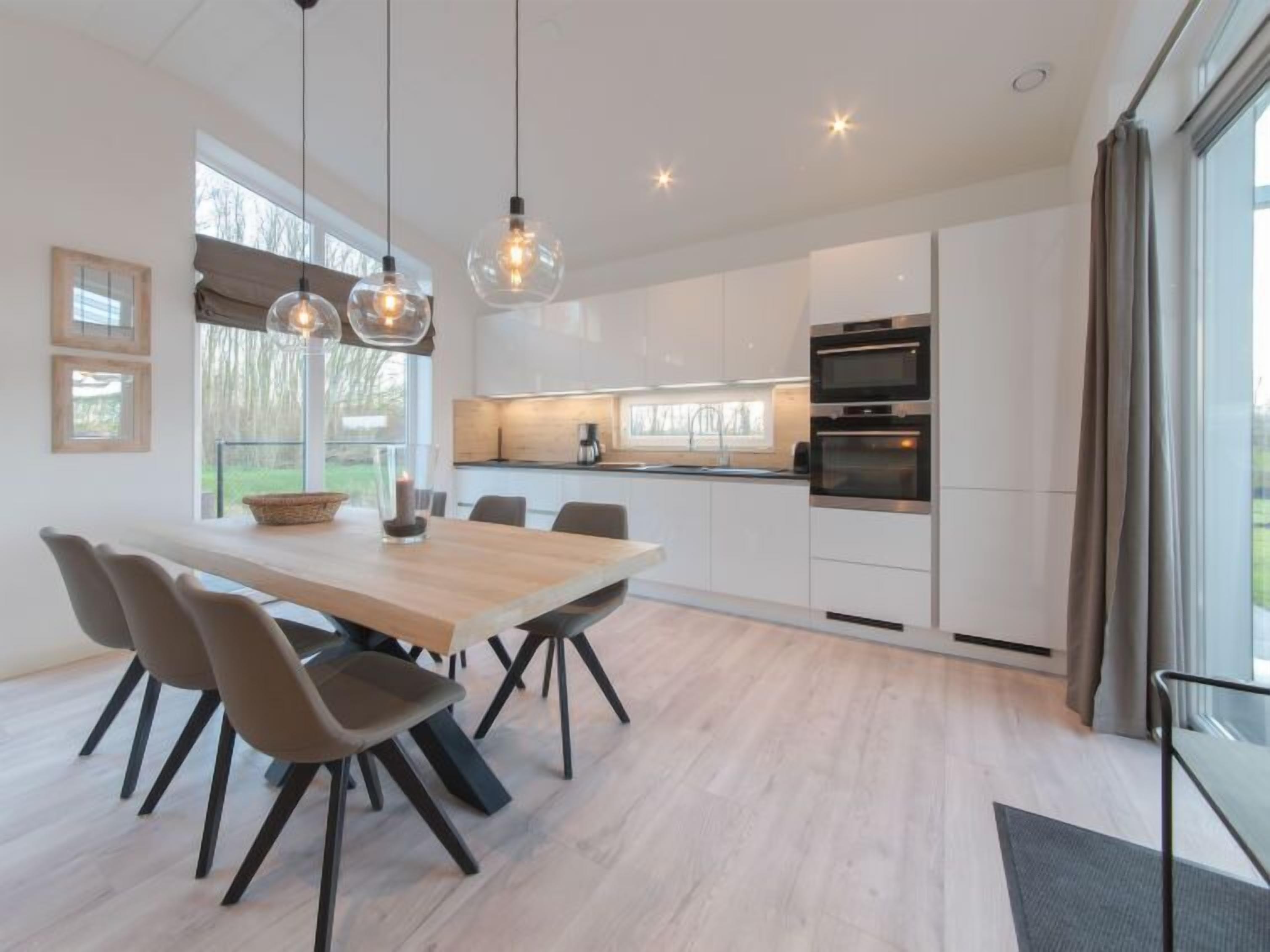 Eine moderne Küche mit weißen Schränken, einem Holztisch mit Stühlen und Pendelleuchten.