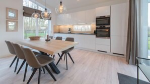 Una cocina moderna con armarios blancos, una mesa de comedor de madera y sillas, y lámparas colgantes.