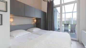 Ein modernes Schlafzimmer mit einem großen Bett, einer Kronleuchter und Blick ins Freie durch große Fenster.