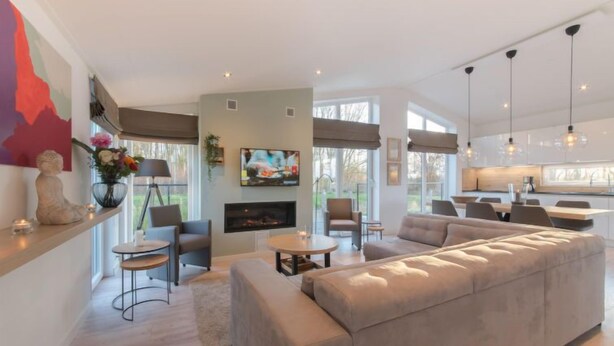 Una sala de estar moderna con un sofá seccional beige grande, una chimenea y un televisor montado en la pared. Hay dos sillones y una mesita en la habitación.