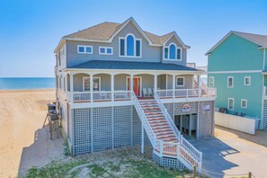 Une maison située en bord de mer, dotée d’un porche couvert, d’un escalier menant à l’étage principal et offrant une vue sur l’océan.
