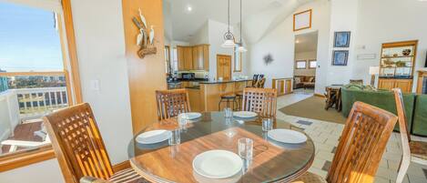 A spacious dining area with a round glass table, wooden chairs, and a view of the kitchen and living room in the background.